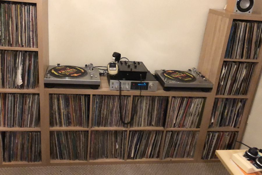 Twin turntables and mixer surrounded by shelves of vinyl records